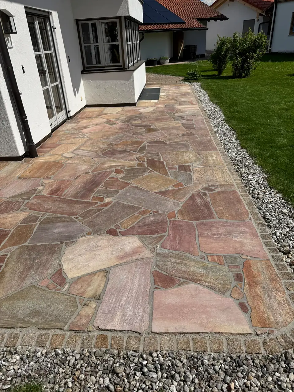 Terrasse aus rötlichen Polygonalplatten mit Granitpflaster-Einfassung am Haus